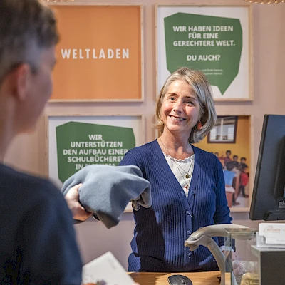 Weltladen-Mitarbeiterin verkauft einer Kundin Fair Fashion